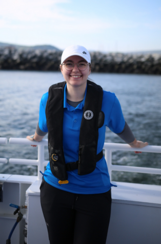 Photo d'Elizabeth Simard, debout dans un bateau, porte un chandail bleu et une veste de flottaison noire